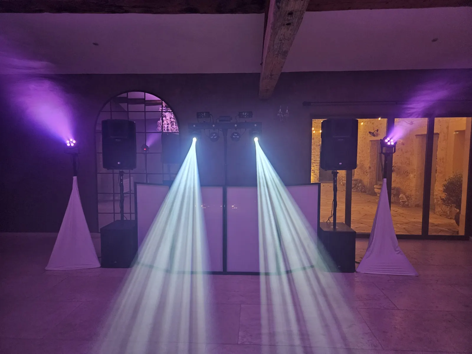Cabine DJ de Nico en salle de réception, entre deux enceintes, sous deux faisceaux de lumière blanche